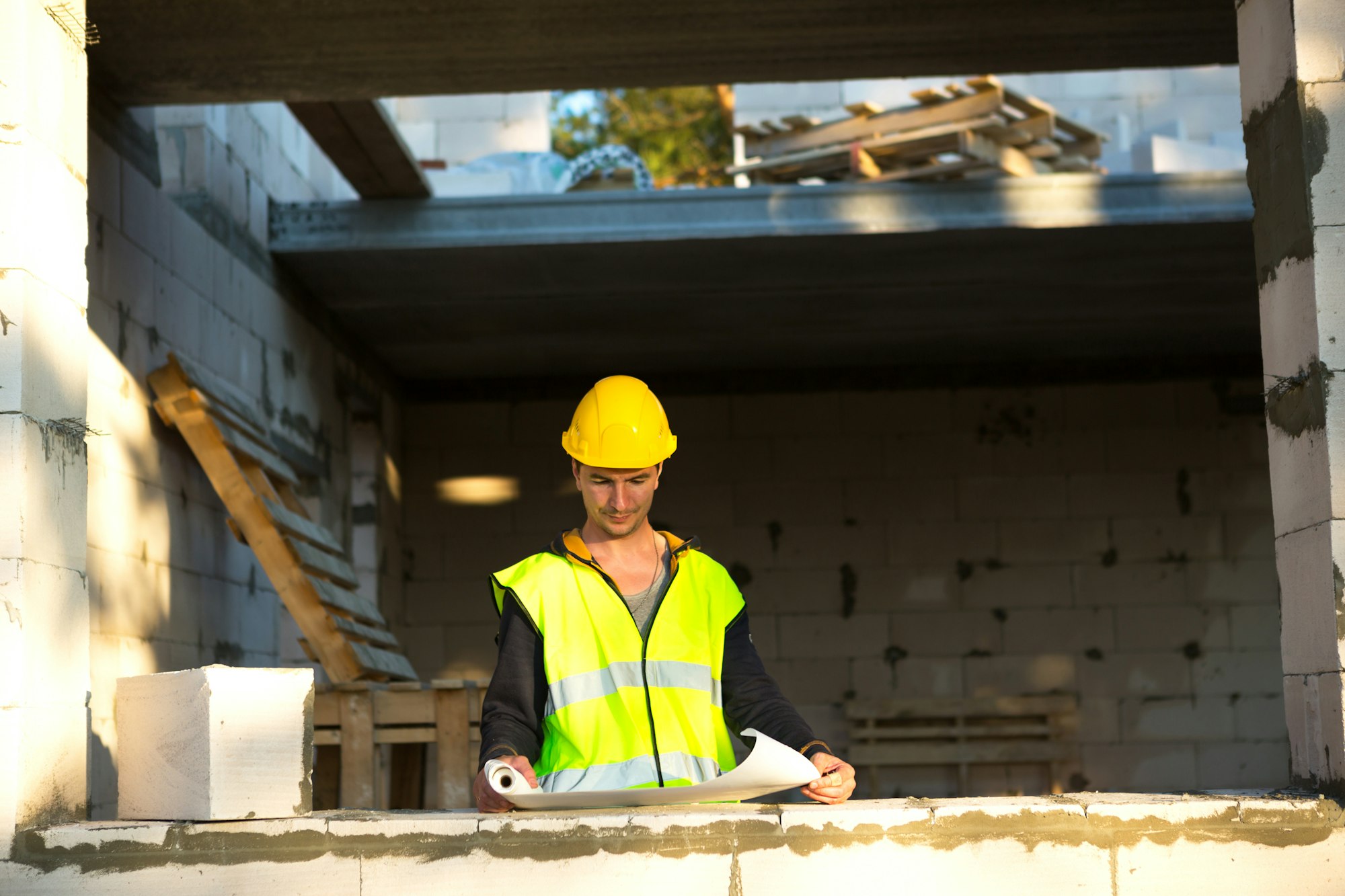 A construction engineer and designer in a yellow hardhat studies a drawing of a building